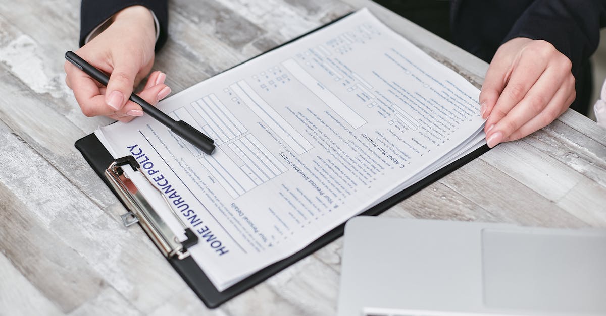 Hands reviewing a commercial insurance policy document on a desk, marking up fields for completion.