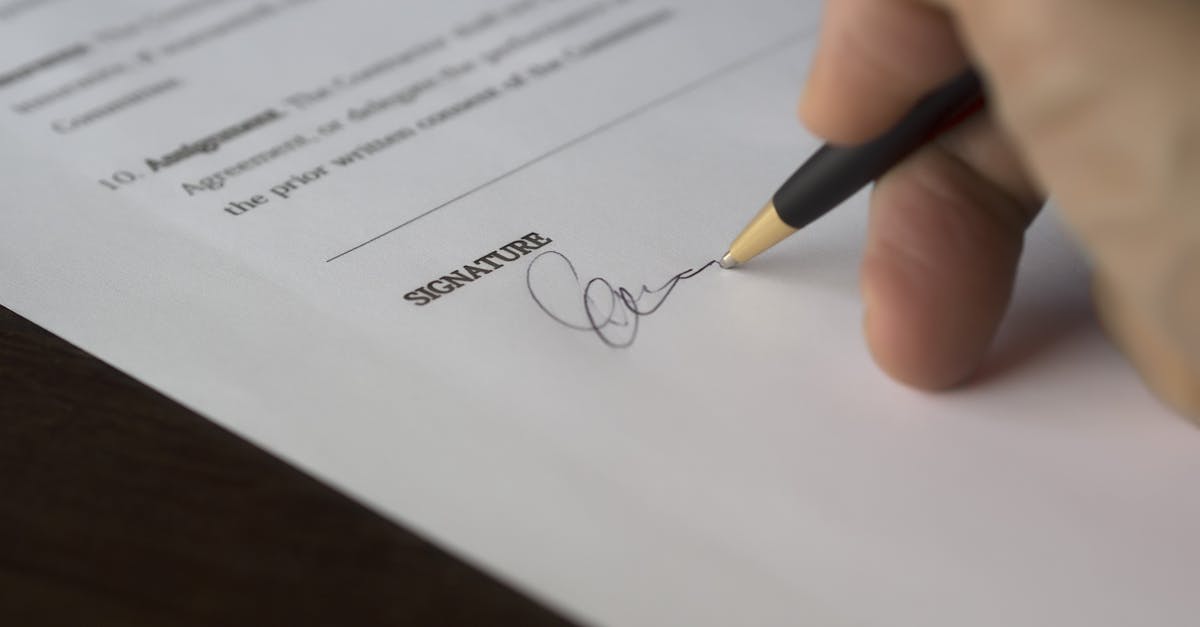 A hand signs a formal insurance certificate document with a pen on a wooden desk.