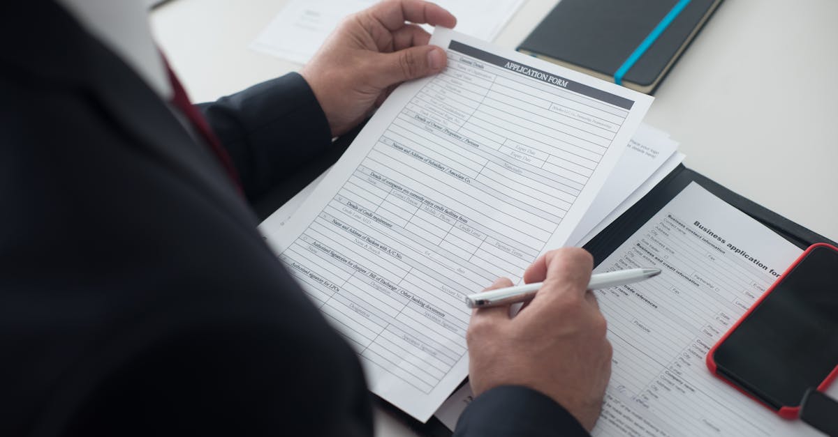 A person in a dark suit reviews a printed visa application form on a desk with a pen, preparing to fill it out.