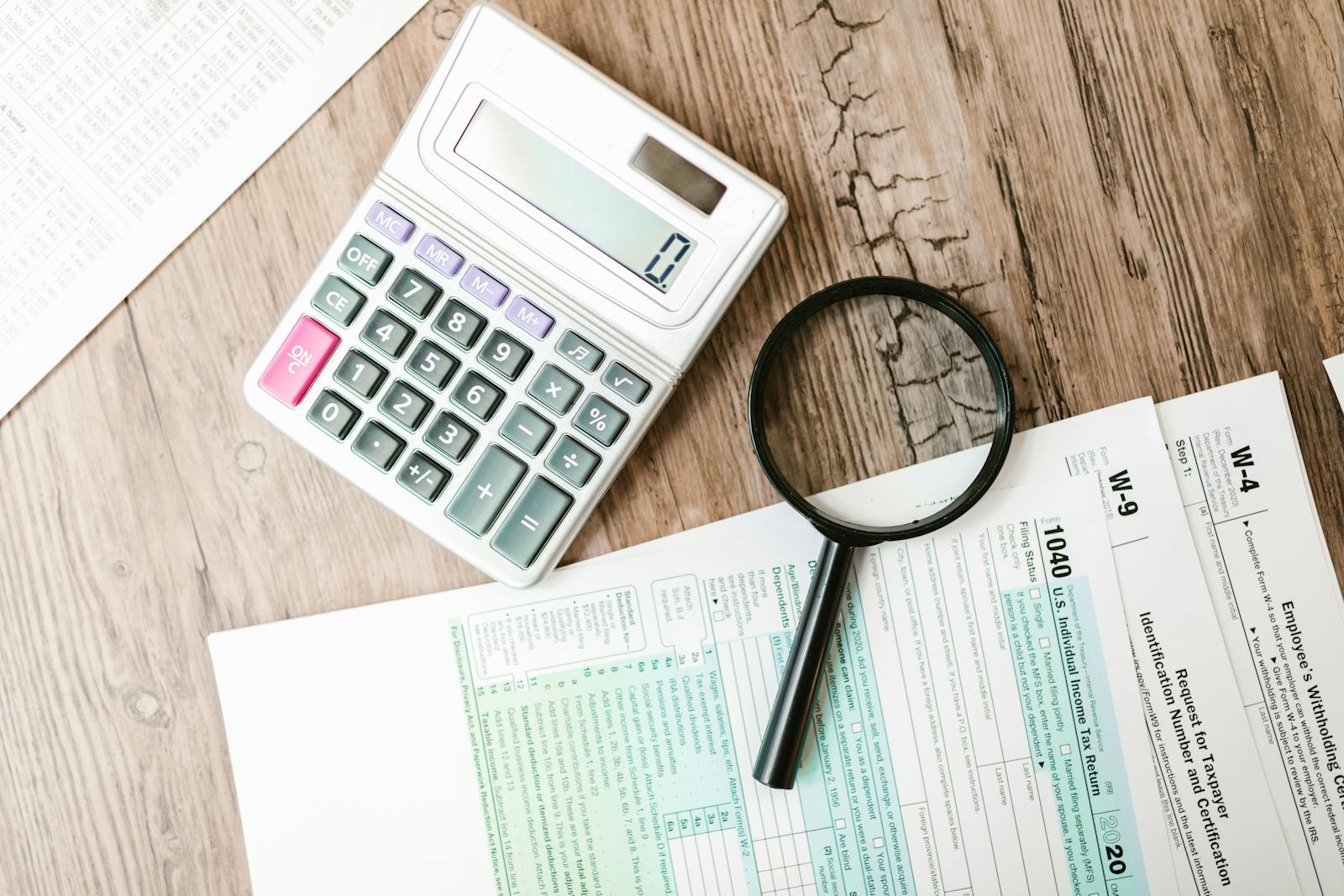 Top-down view of German tax forms on a wooden desk with a calculator, magnifying glass, and pen during tax season.